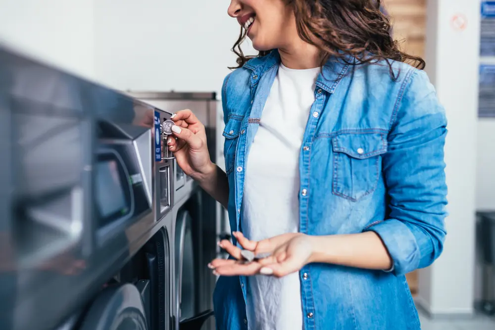 Woman loading clothes into a front-loading commercial coin-operated washing machine