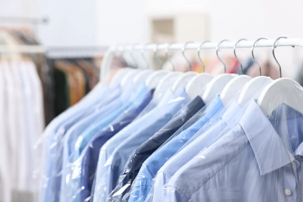Row of freshly dry cleaned dress shirts in individual protective plastic covers hanging neatly on a garment rack