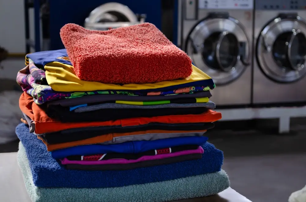 A stack of neatly folded colorful towels on a table in front of laundromat washing machines